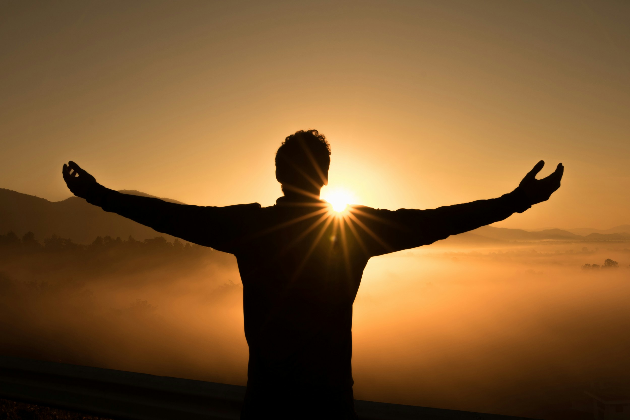 Sunshine glowing behind a man with outstretched arms